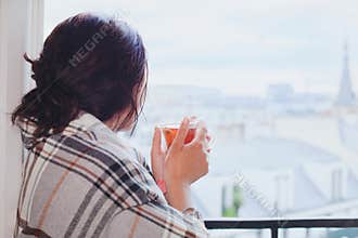 Woman drinking hot tea and looking at the window, cozy winter at home