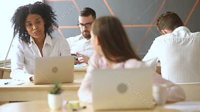 Woman working on laptop, talking to african colleague in coworking