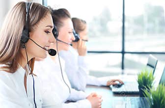 Portrait of smiling female customer service agent wearing headset with colleagues working in background at office.