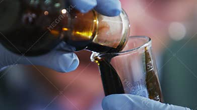 Assistant Pours Raw Oil from Bulb into Lab Glass