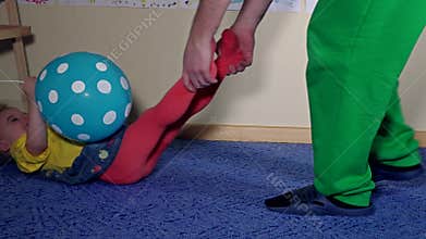 Playful dad pulling his funny daughter by legs through carpet on floor