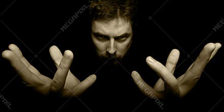 Hands and face of evil magician in the dark