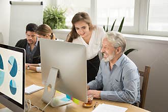 Smiling young manager helping senior worker with computer office