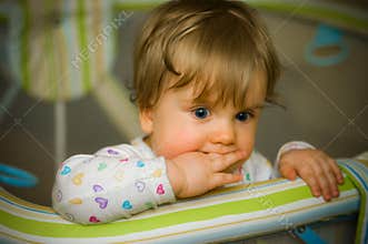 Thoughtful baby in playpen biting her fingers