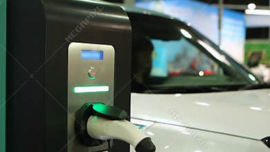 Woman testing e-car, electric vehicle showroom, auto plugged in charging point