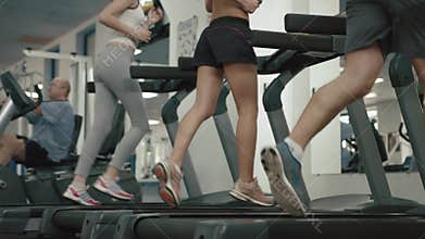 Unknown athletic people in sportswears are warming up by running on the treadmill. 4k footage. No face. Gym location.