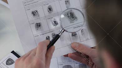 Police officer checking fingerprints file with magnifying glass, identification