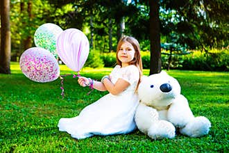Happy little girl with many balloons and a teddy bear