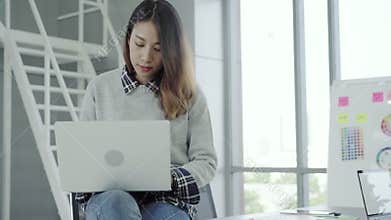 Young Asian female manager using portable computer device while sitting at modern workplace.