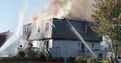 Blazing house fire. Firefighters spray water on house with hose.