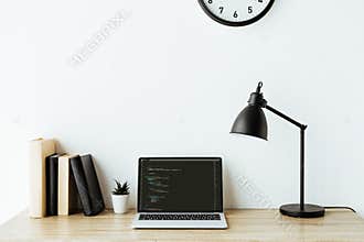laptop with program code and books on work desk