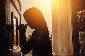 Silhouette of woman kneeling and praying in modern church at sun