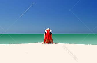 Woman in Red hat and bikini sitting all alone on empty beach