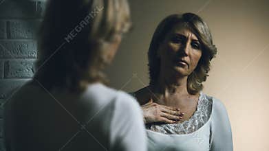 Sad senior female looking in mirror with disgust, aging problem, insecurities