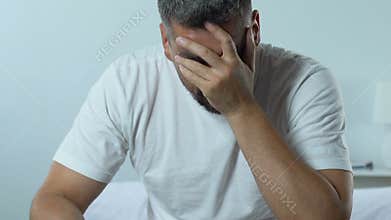 Sad handsome man sitting on bed holding pills blister, mens health problem