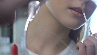 Young lady applying lipstick looking in mirror and smiling, preparing for date