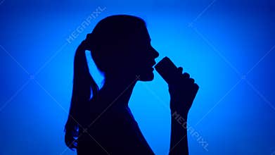 Silhouette of woman open can of soft drink on red background. Female`s face in profile drink soda