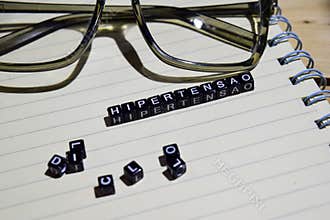Concept of Hipertensao in spanish on wooden cubes with glass eye, books in Vintage background