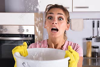 Woman Holding A Bucket While Water Droplets Leak From Ceiling