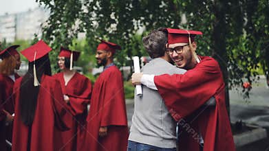 College professor is congratulating his student after graduation ceremony hugging him and shaking hand, teacher is proud