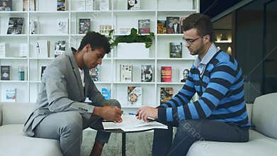 Men making deal and signing papers. Side view of diverse men signing contract and shaking hands in symbol of agreement