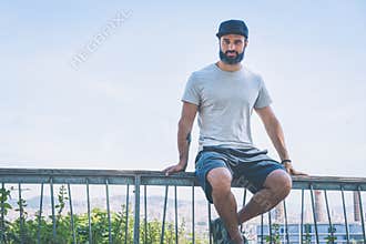Bearded muscular hipster man model wearing gray blank t-shirt and a black baseball cap with space for your logo or
