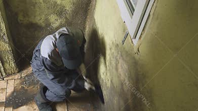 The man cleans the walls of strong dirt with a brush and a rag. The worker washes the corridor walls manually. Mold and