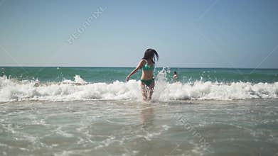 Pretty woman with dark hair and perfect body wearing sunglasses and bikini runs away from the sea wave. Cute young babe