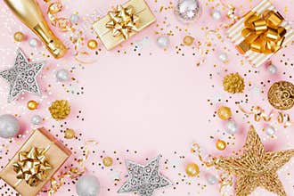 Christmas background with gift or present box, champagne, confetti and holiday decorations on pink pastel table top view. Flat lay
