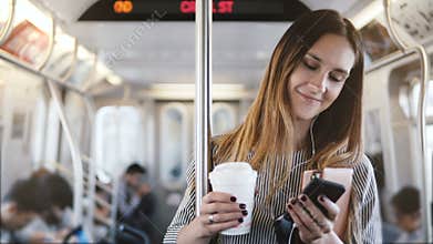 Happy relaxed beautiful millennial girl stands in subway train looking at smartphone using e-commerce mobile app smiling