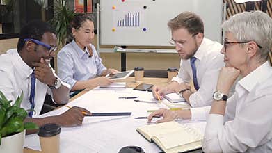 Multiracial architect colleagues brainstorming building blueprints in office.