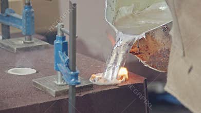Workers in a foundry pouring liquid Aluminum to a sand cast