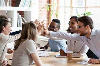 Excited multiracial team giving high five at company meeting
