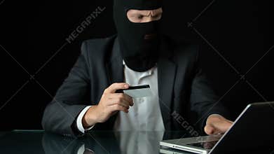 Man in balaclava and suit committing bank fraud, using stolen credit card, crime