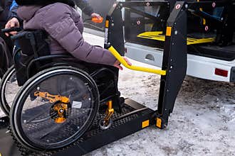 A man presses a button on the control panel to pick up a woman in a wheelchair in a taxi for the disabled. Black lift specialized