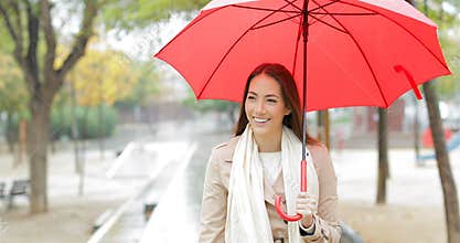 Happy woman walking holding an umbrella under the rain