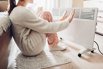 Using heater at home in winter. Woman warming her hands. Heating season.