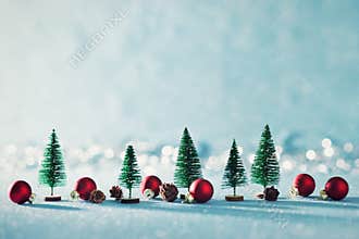 Magical miniature winter wonderland background. Evergreen trees, pine cones and red christmas baubles on shiny blue background.