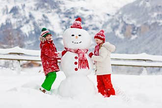 Child building snowman. Kids build snow man. Boy and girl playing outdoors on snowy winter day. Outdoor family fun on Christmas