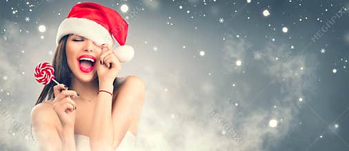 Christmas woman. Joyful model girl in Santa`s hat with red lips and lollipop candy in her hand