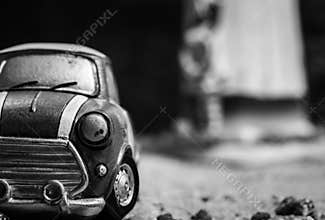 Front view of small car toy model on sand road. Black and white mini car toy on blurred background. Cartoon miniature car.