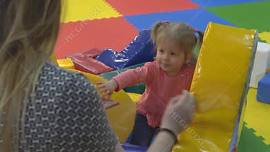 Young mother and daughter are playing in the playroom, climbing on an inflatable hill