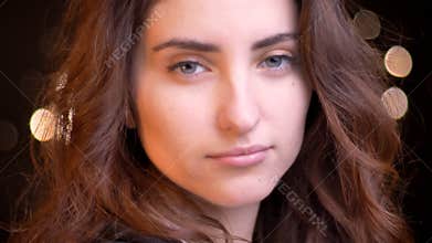 Closeup shoot of young attractive caucasian female face looking straight at camera with bokeh lights on the background