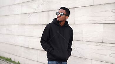 Portrait african man in black hoodie, sunglasses walking on city street looking away
