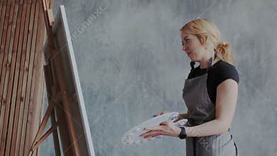 Cheerful woman creates artwork. She painting pictures in modern loft minimalist interior. She drawing acrylic with full