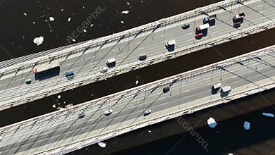 Aerial view of trucks and cars driving on a cable-stayed bridge over the river