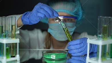 Lab assistant adding green powder to tube with green plant, fertilizer influence