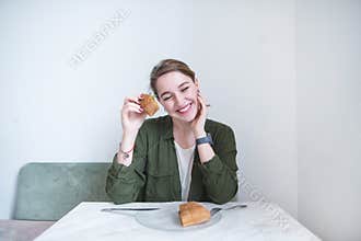A girl with a sandwich in her hands sincerely smiles while sitting at the restaurant table