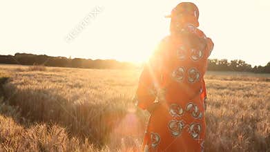 Rear View of African woman in traditional clothes standing in a field of crops at sunset or sunrise