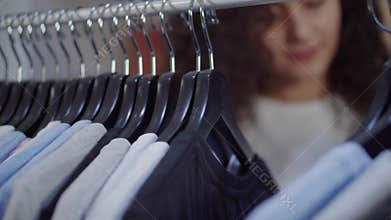 Shopper is moving hangers with tee shirts in sportive clothing store, close-up